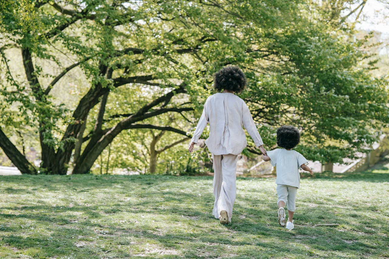 Mom and child walking hand-in-hand in a sunny park setting, showcasing family bonding and nature.