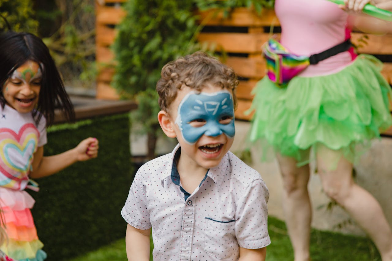 Children having fun with face painting at a lively outdoor birthday party.